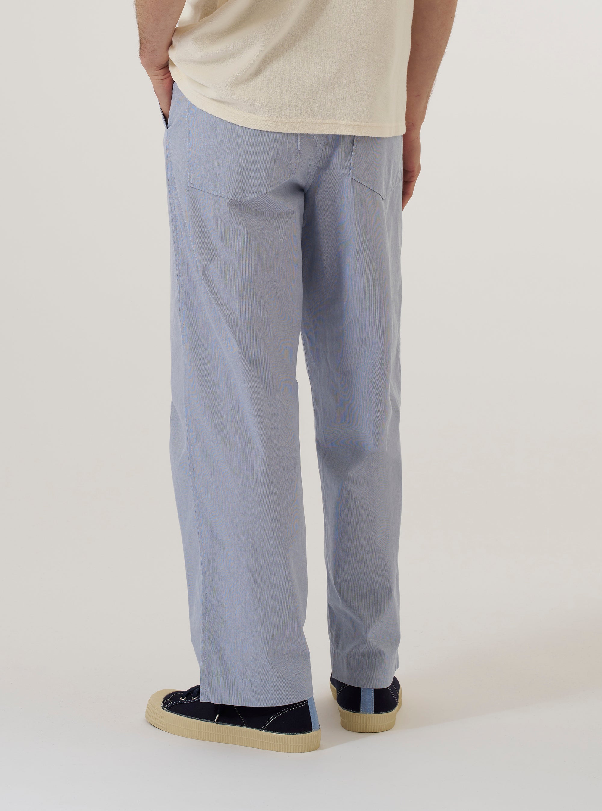 A model wears the Navy Kennedy Stripe Duke Pant, shown from a rear three-quarter angle against a plain, neutral studio background. The trousers feature a loose, wide-leg fit and a distinct vertical stripe pattern on a navy blue cotton base. A single patch pocket is visible on the rear, and the garment has a relaxed, pleated construction.