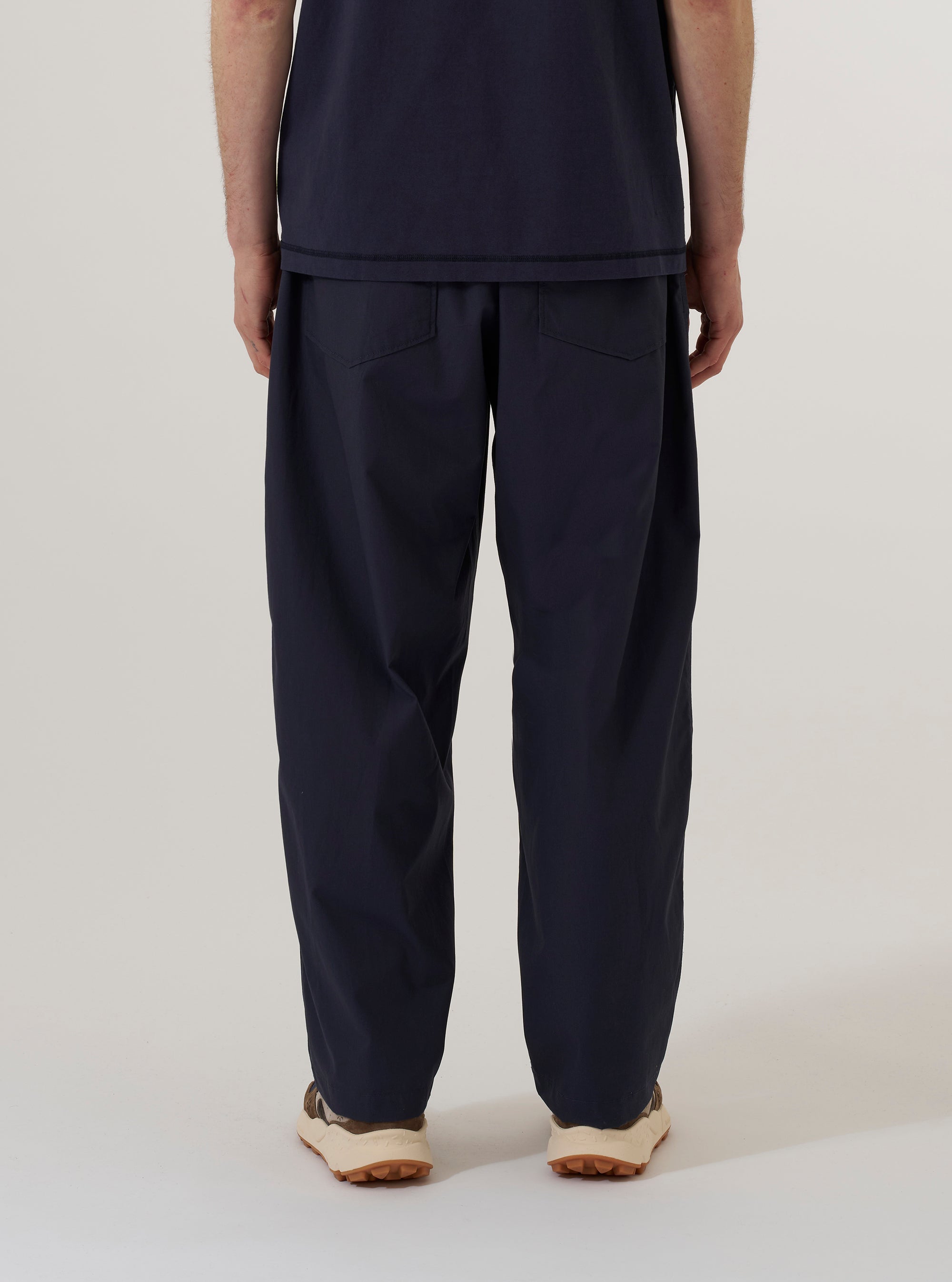 A model wears the Navy Peached Poplin Dutch Pant, shown from the waist down from a rear three-quarter angle against a plain white background. The image highlights the exceptionally wide leg, the soft matte texture of the navy peached poplin fabric, and a rear patch pocket. The model is also wearing dark shoes.