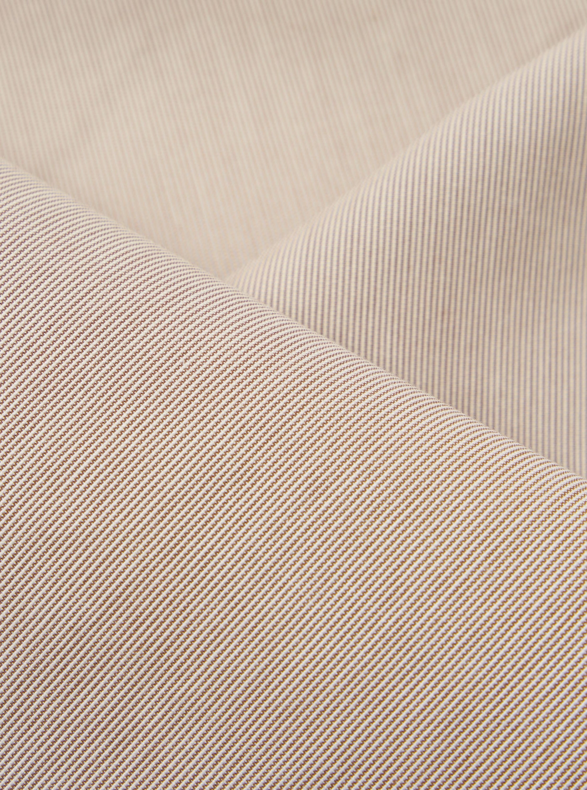 A close-up fabric swatch of the Brown Kennedy Stripe Hi Water Trouser highlights the brown vertical stripe pattern and the texture of the cotton fabric. The material fills the frame, providing a detailed view of the garment's color and construction.