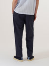 A model wears the Navy Peached Poplin Judo Pant, shown from the waist down against a plain white background. The image highlights the relaxed, straight-leg fit and the elasticated waistband with an external drawcord. The navy blue cotton fabric has a soft, matte finish. The model is wearing the trousers with a pair of dark shoes.