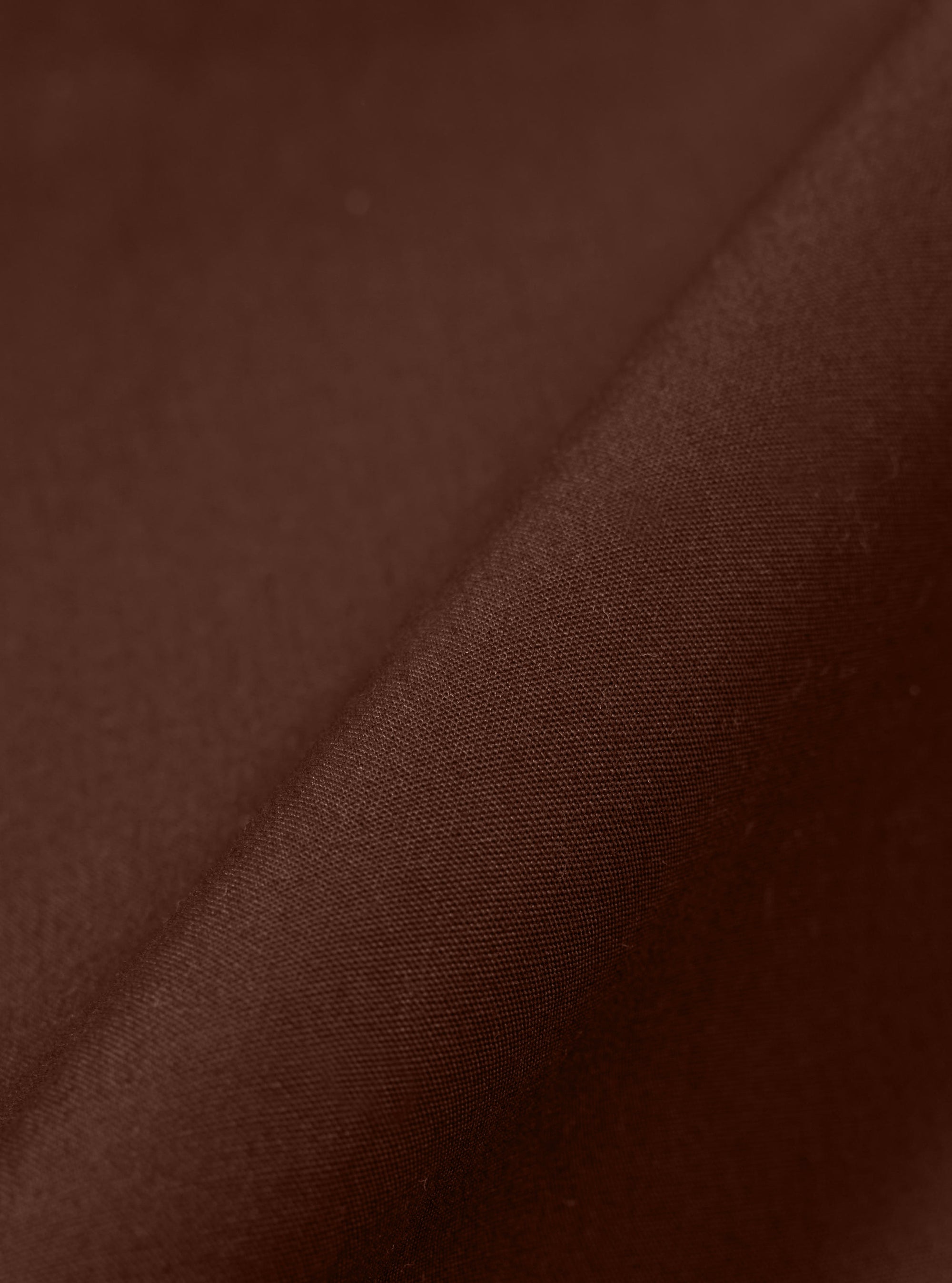A close-up fabric swatch of the Brown Peached Poplin Judo Pant is shown, highlighting the warm, earthy brown color and the smooth, tightly woven texture of the cotton poplin fabric. The lightly brushed, peached finish is visible across the material.