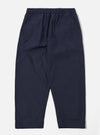 The Navy Peached Poplin Judo Pant is shown as a flat lay against a white background. The trousers feature a relaxed, wide-leg fit with a distinctive wrap-front waist, an integrated drawstring, and a single large patch pocket on the right leg. The fabric has a smooth, matte finish characteristic of peached poplin.