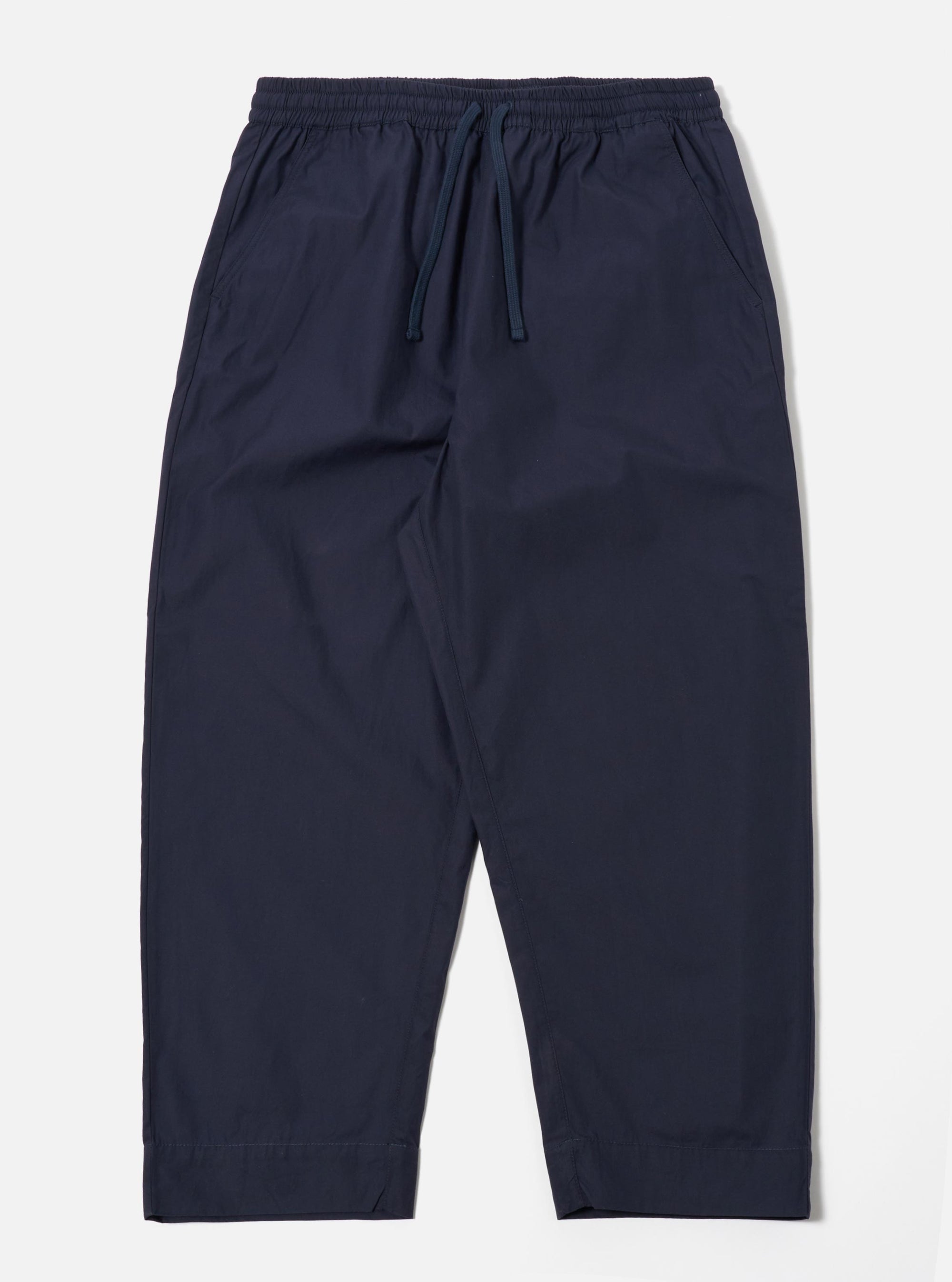 The Navy Peached Poplin Judo Pant is shown as a flat lay against a white background. The trousers feature a relaxed, wide-leg fit with a distinctive wrap-front waist, an integrated drawstring, and a single large patch pocket on the right leg. The fabric has a smooth, matte finish characteristic of peached poplin.