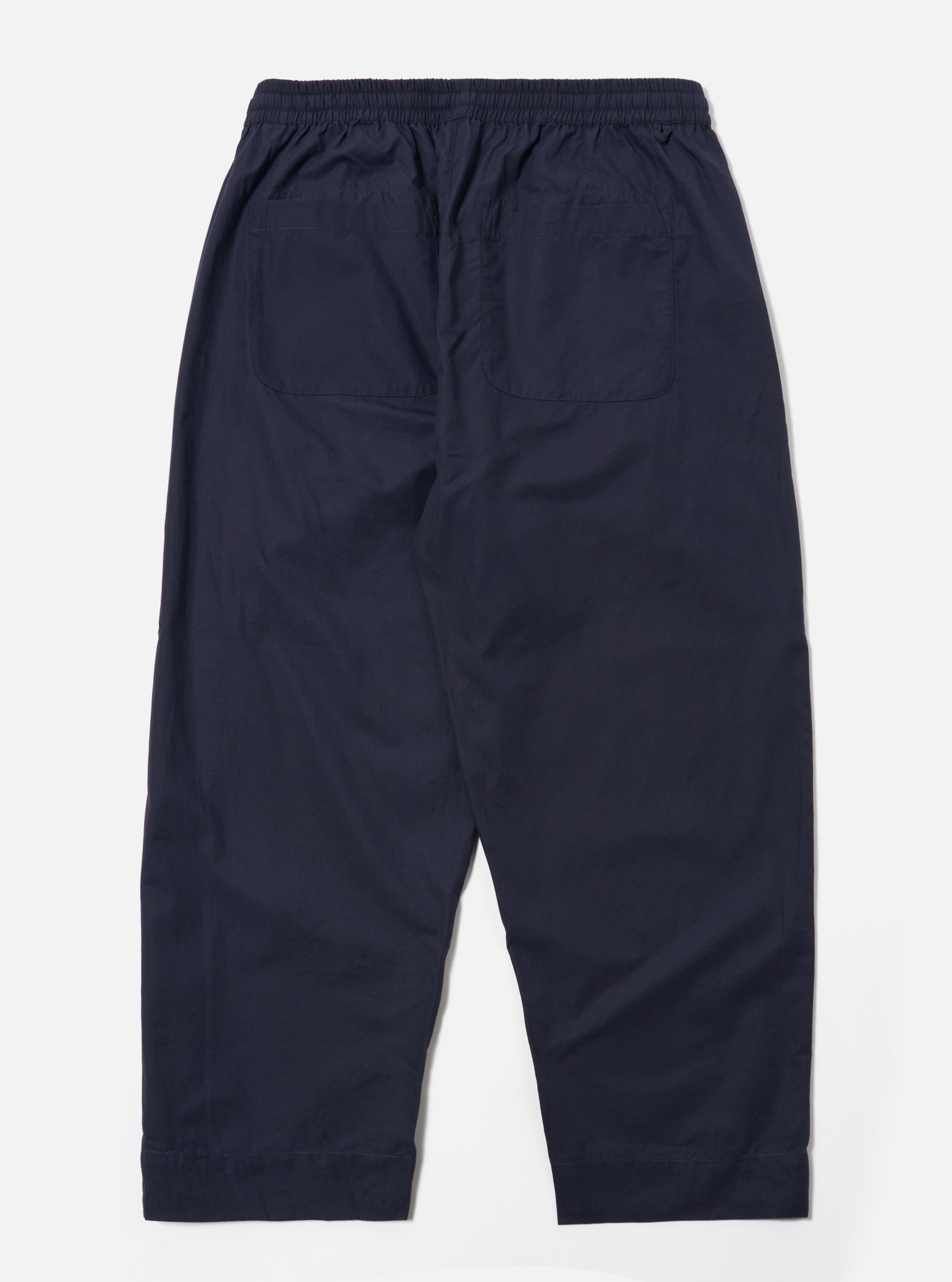 The Navy Peached Poplin Judo Pant is shown from the rear in a flat lay against a plain white background. The image highlights the back of the trousers, showing a single rear patch pocket on the right side and an elasticated waistband with internal drawstring detailing. The peached poplin fabric appears smooth and matte in a deep navy blue. No model or mannequin is present.