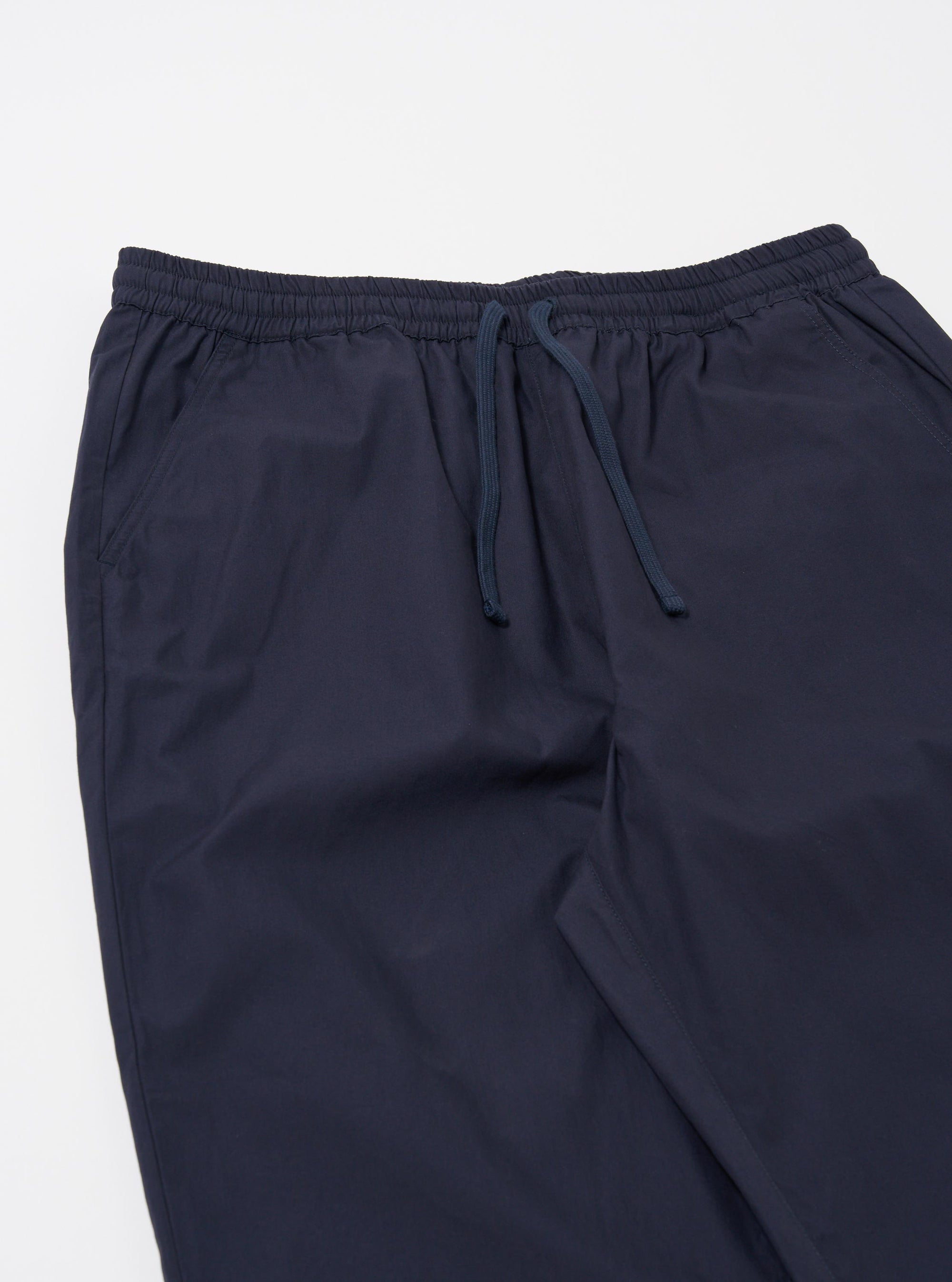 The Navy Peached Poplin Judo Pant is shown as a flat lay against a plain white background. The image focuses on the rear of the trousers, highlighting two large, asymmetrical patch pockets and a comfortable elasticated waistband with an internal drawstring. The fabric appears smooth with a soft, peached finish.