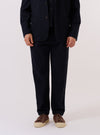 A model wears the Dark Navy Ospina Cotton Military Chino against a plain, neutral background. The image highlights the mid-rise, tapered-leg silhouette and the visible puckered texture of the dark navy seersucker fabric. The model is shown from the waist down, wearing the trousers with a tucked-in shirt to display the waistband and front pocket details.