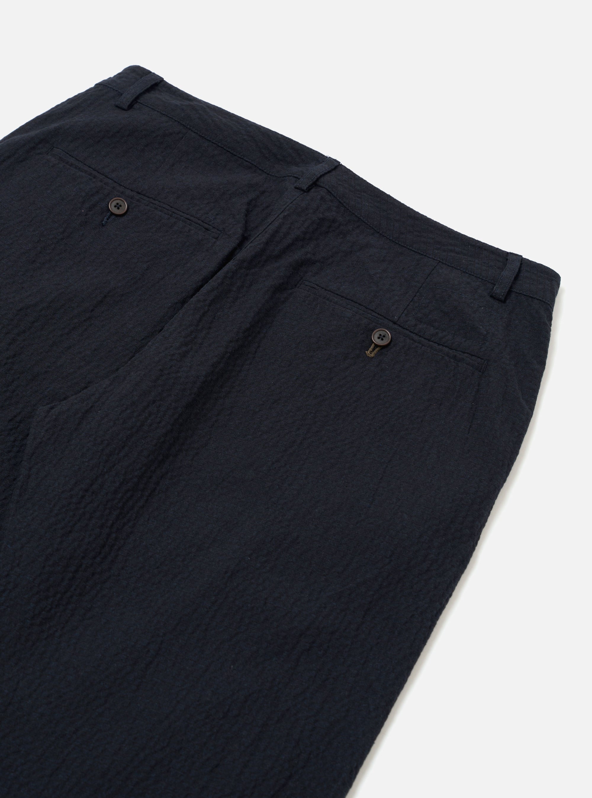 The Dark Navy Ospina Cotton Military Chino is shown in a detail view as a flat lay against a plain white background. The image highlights the textured seersucker finish of the dark navy fabric and the construction of the pockets and waistband.