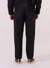 A model wears the Black Recycled Polytech Military Chino, shown from the waist down against a plain white background. The trousers feature a slim, straight-leg fit and are made from a smooth black recycled polytech fabric. The image highlights the clean, military-style construction and the technical texture of the material.