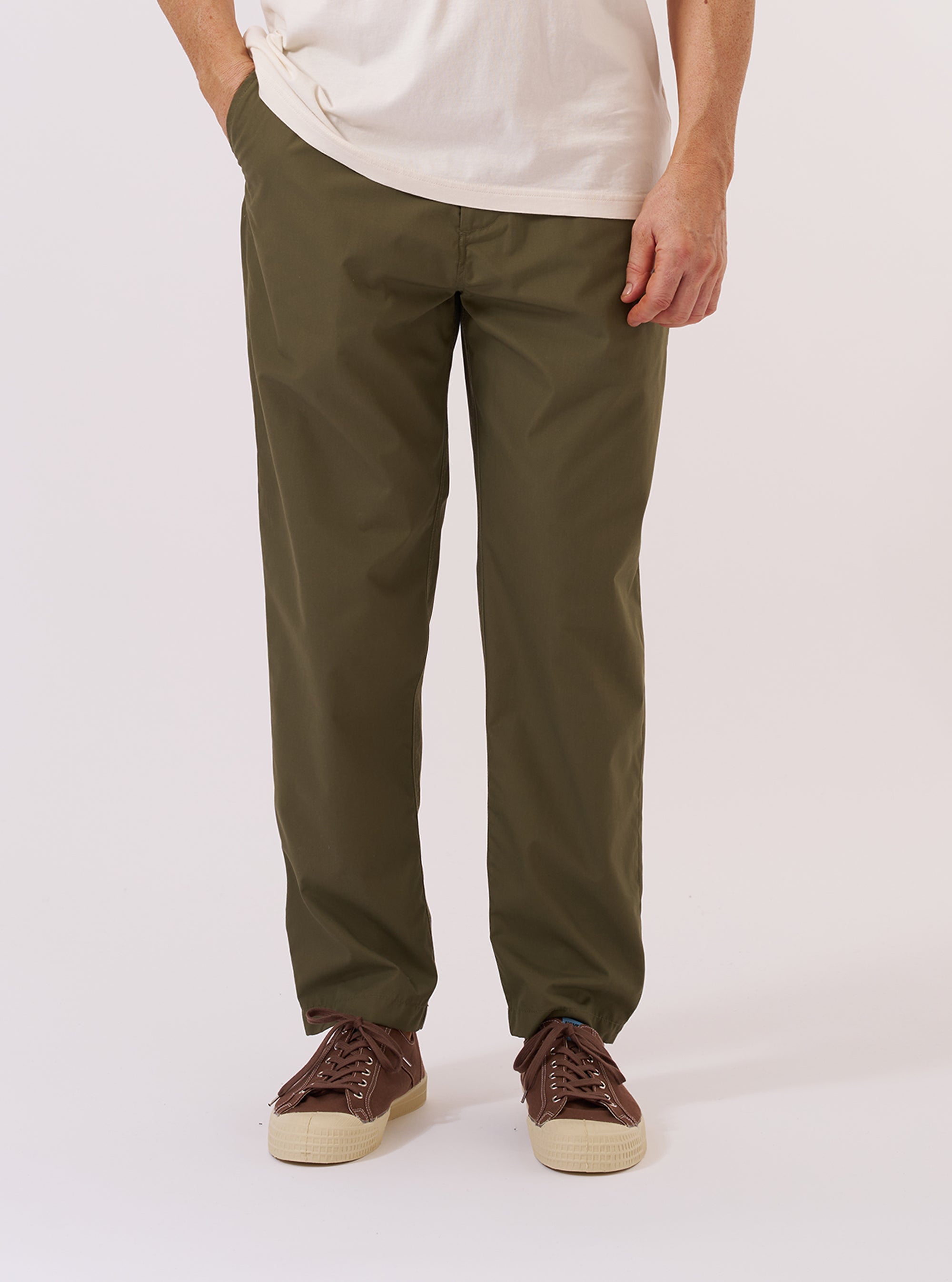 A model is wearing the Olive Recycled Polytech Military Chino, shown from the waist down against a plain white background. The olive green trousers feature a contemporary slim-straight fit, a button fly, and two side pockets. The model is wearing a light-colored top and white socks with black shoes to highlight the clean lines and tapered leg of the chinos.