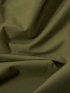 A close-up fabric swatch of the Olive Recycled Polytech Parachute Short is shown, highlighting the smooth, matte texture and deep olive green color of the recycled polytech material.