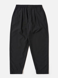 The Black Tropical Suiting Pleated Track Pant is shown as a flat lay against a plain white background. The trousers feature an elasticated waistband with an internal drawstring, a single front pleat on each leg, and two side pockets. The black tropical suiting fabric is a lightweight polyester and wool blend with a smooth finish.