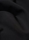 A close-up fabric swatch of the Black Tropical Suiting Pleated Track Pant is shown, highlighting the fine, smooth texture and solid black color of the lightweight tropical suiting material.
