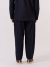 A model is wearing the Navy Tropical Suiting Pleated Track Pant, shown from the waist down against a plain white background. The image highlights the loose, tapered fit of the trousers and the single pleat at the front. The model is wearing the pants with a white t-shirt tucked into the elasticated waistband and white socks. The navy blue fabric appears smooth and lightweight.