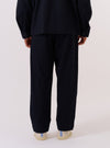 A model wears the Dark Navy Ospina Cotton Oxford Pant, shown from a rear three-quarter angle against a plain white background. The image highlights the loose, wide-leg fit of the trousers and the puckered seersucker texture of the dark navy fabric. The model is wearing the pants with a matching dark navy jacket and white shoes.