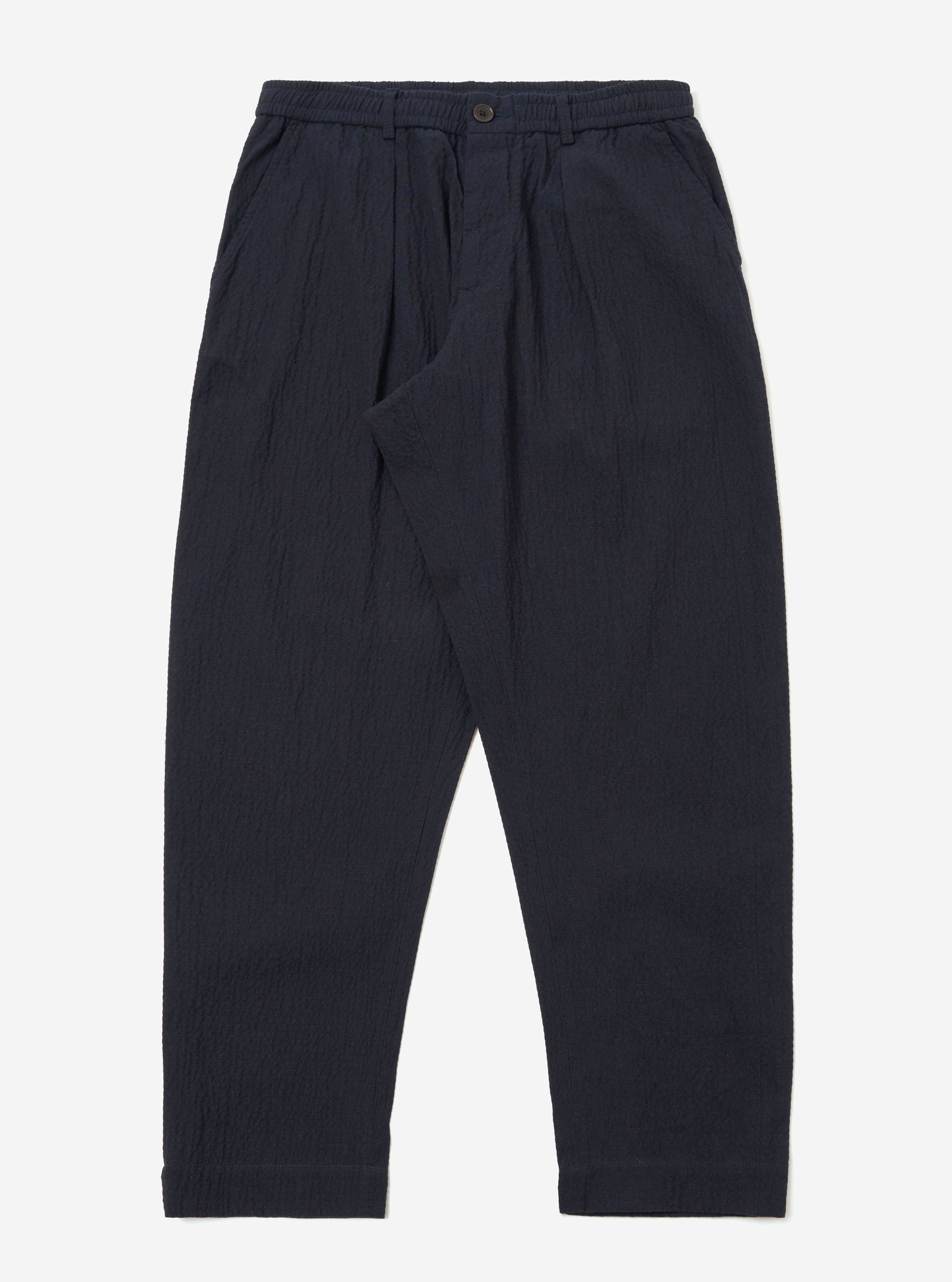 The Dark Navy Ospina Cotton Oxford Pant is shown as a flat lay against a white background. The trousers feature a single pleat at the front, a button fly, and an elasticated waistband with an external drawstring. The dark navy fabric has a visible puckered seersucker texture throughout.