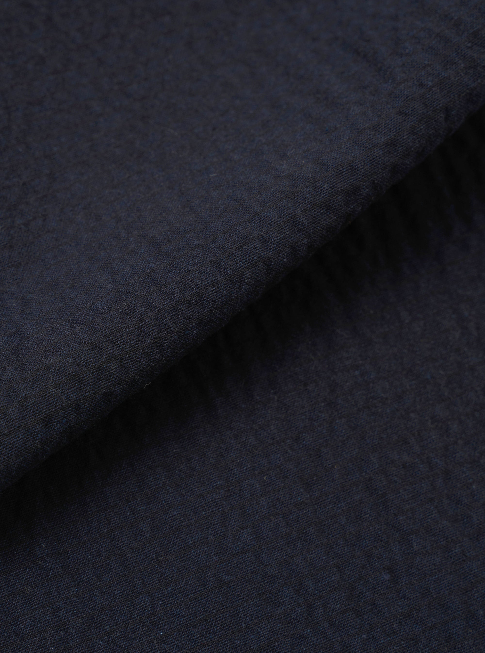 A close-up fabric swatch of the Dark Navy Ospina Cotton Oxford Pant highlights the deep navy blue color and the distinct puckered texture of the seersucker fabric. The material fills the frame, providing a detailed view of the garment's weave and finish.