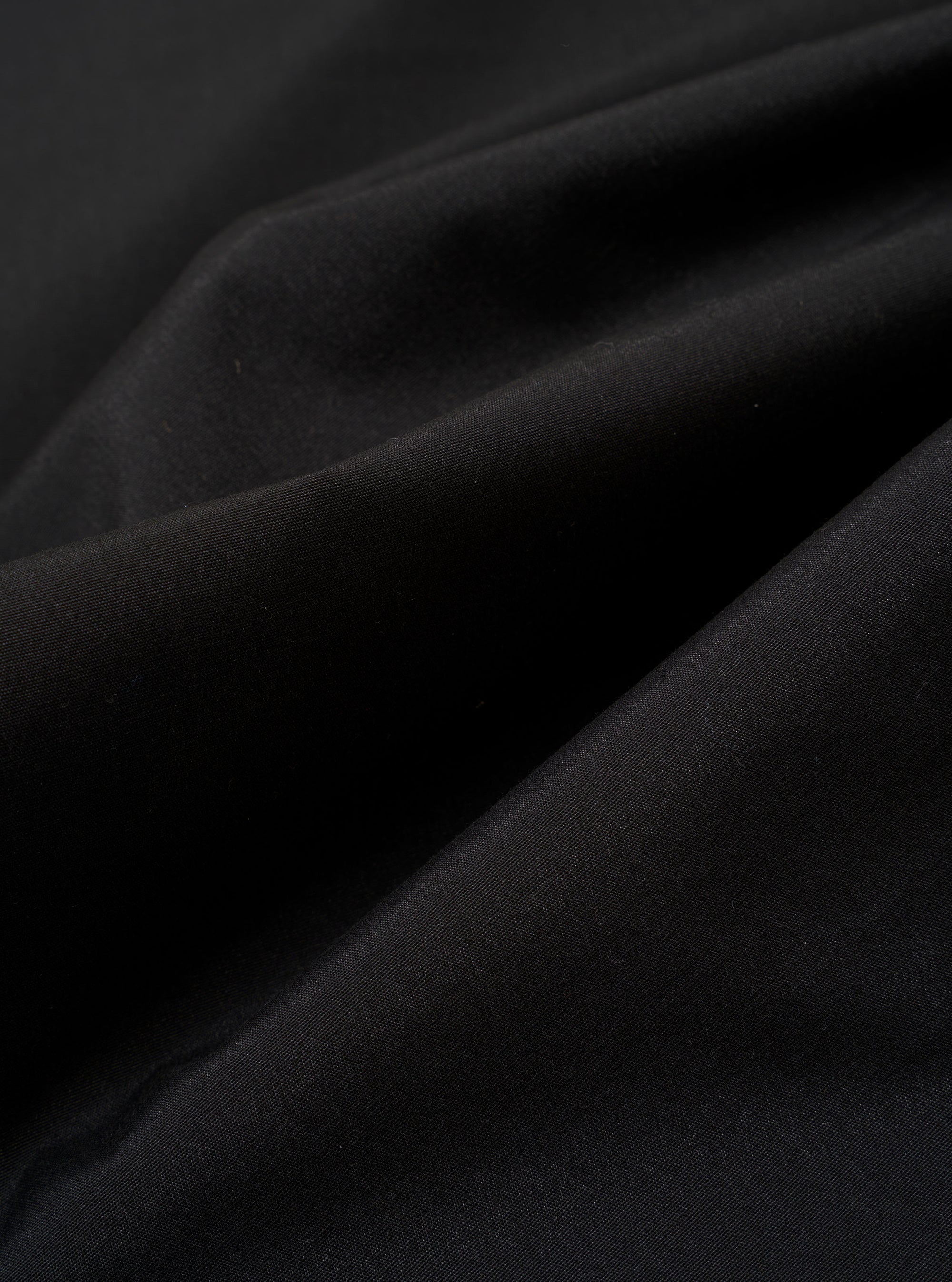 The Black Recycled Polytech Pleated Track Pant is shown in a close-up detail shot against a plain white background. The image focuses on the rear of the garment, highlighting the clean construction of the elasticated waistband and a single rear patch pocket. The black recycled polytech fabric has a smooth, technical finish with visible tonal stitching.