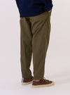 A model wears the Olive Recycled Polytech Pleated Track Pant, shown from a side-angle view against a plain white background. The trousers feature a loose silhouette that tapers toward the hem, a pleated front, and an elasticated waistband. The garment is constructed from a smooth olive green recycled polytech fabric.