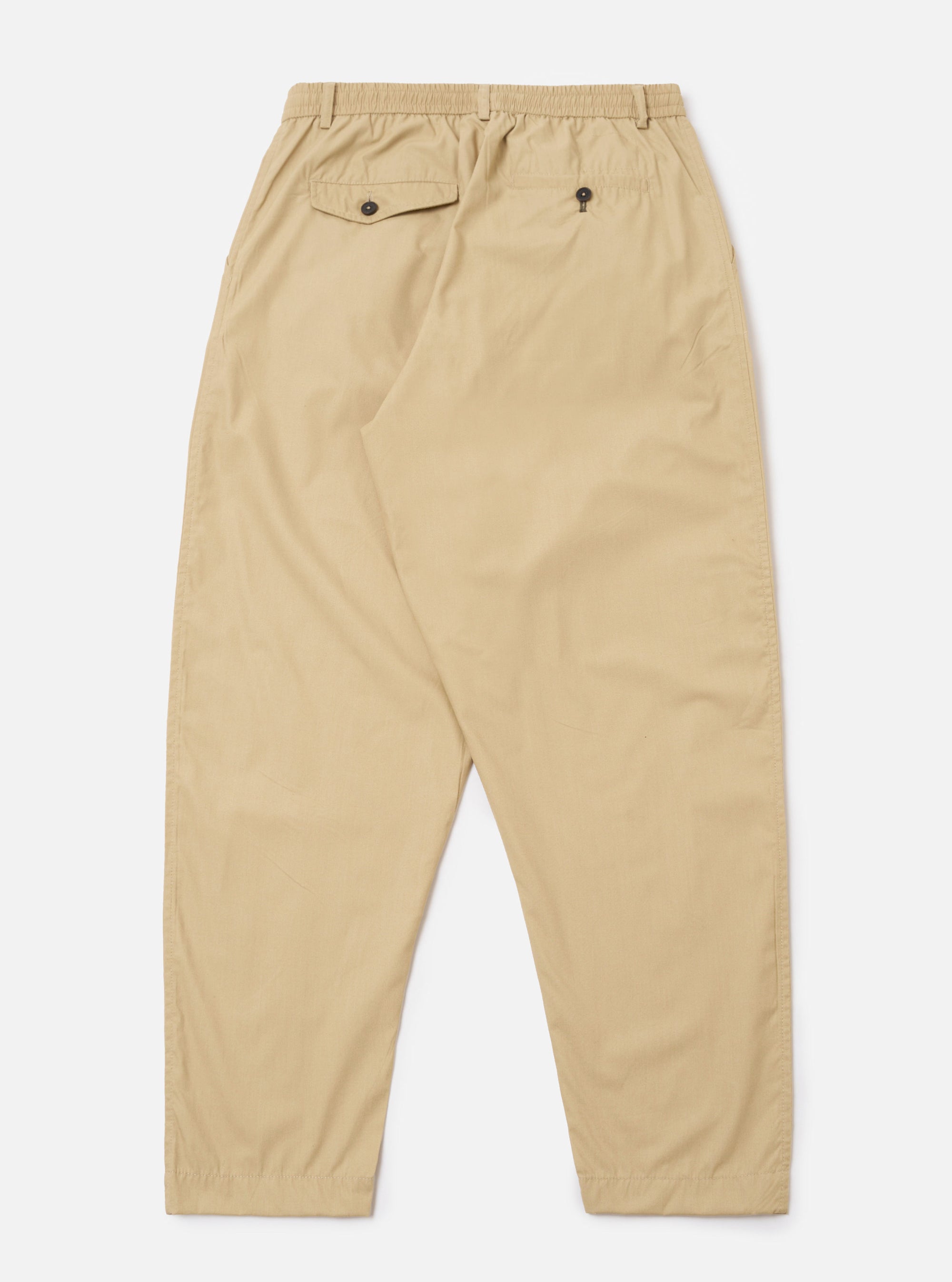 The Sand Recycled Polytech Pleated Track Pant is shown from the back as a flat lay against a plain white background. The image highlights the elasticated waistband and the two rear pockets, including one with a buttoned flap and one jetted pocket with a button closure. The fabric is a smooth, sand-colored recycled polyester and cotton blend.