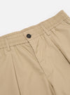 The Sand Recycled Polytech Pleated Track Pant is shown from the back as a flat lay against a plain white background. The image highlights the elasticated waistband and the two rear pockets, including one with a buttoned flap and one jetted pocket with a button closure. The fabric is a smooth, sand-colored technical blend.