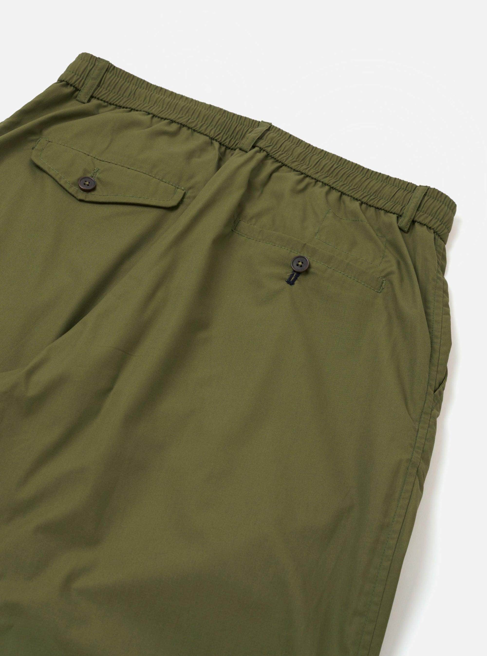 The Olive Recycled Polytech Pleated Track Pant is shown from a rear angle as a flat lay against a plain white background. The image highlights the back of the trousers, featuring two rear pockets—one with a buttoned flap—and the elasticated waistband. The technical olive green fabric has a slight sheen.