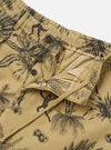 The Sand Jungle Toile Twill Oxford Pant is shown in a detail view as a flat lay against a plain white background. The image highlights the intricate dark jungle toile print featuring tropical foliage and animals on a sand-colored base, as well as the construction of the single pleat at the front.