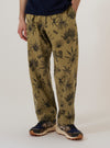 A model wears the Sand Jungle Toile Twill Oxford Pant, shown from the waist down against a plain white background. The trousers feature a loose, wide-leg fit with a single pleat at the front and a drawstring waistband. The sand-colored cotton twill fabric is covered in a dark jungle toile print featuring various animals and tropical foliage. The model is also wearing a light-colored shirt and dark loafers.