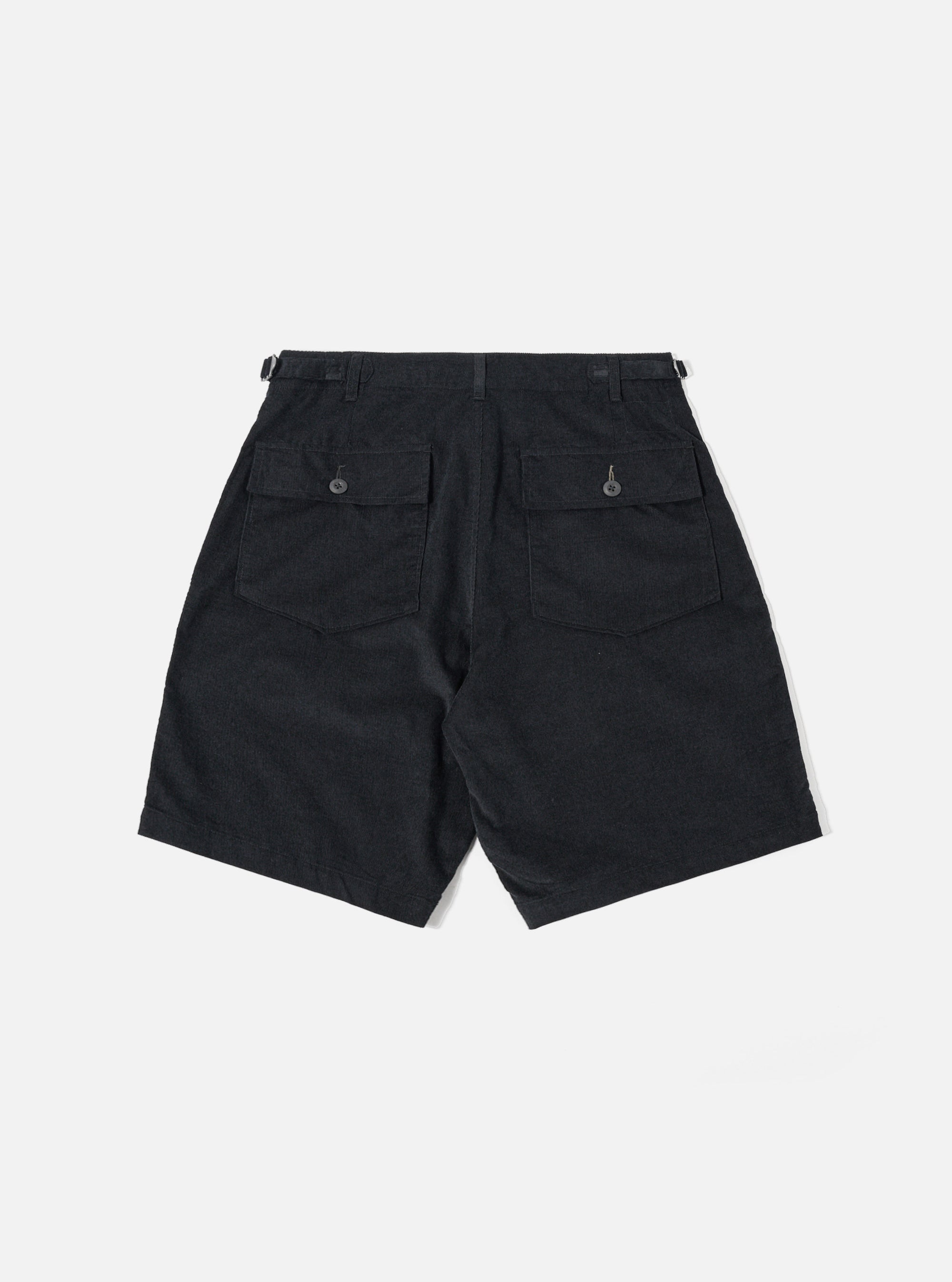 The Black Organic Fine Cord Fatigue Short is shown from the back as a flat lay against a plain white background. The shorts feature a single rear patch pocket on the right side with a button-down flap and two visible metal eyelets at the bottom. The black organic cotton corduroy fabric has a fine vertical wale texture and an elasticated waistband.