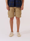 A model wears the Sand Recycled Polytech Parachute Short over a white long-sleeved shirt against a plain white background. The image shows a front view of the shorts, highlighting the relaxed fit, knee-length cut, and large military-style bellows pockets on the sides. The elasticated waistband with a drawstring is also visible.