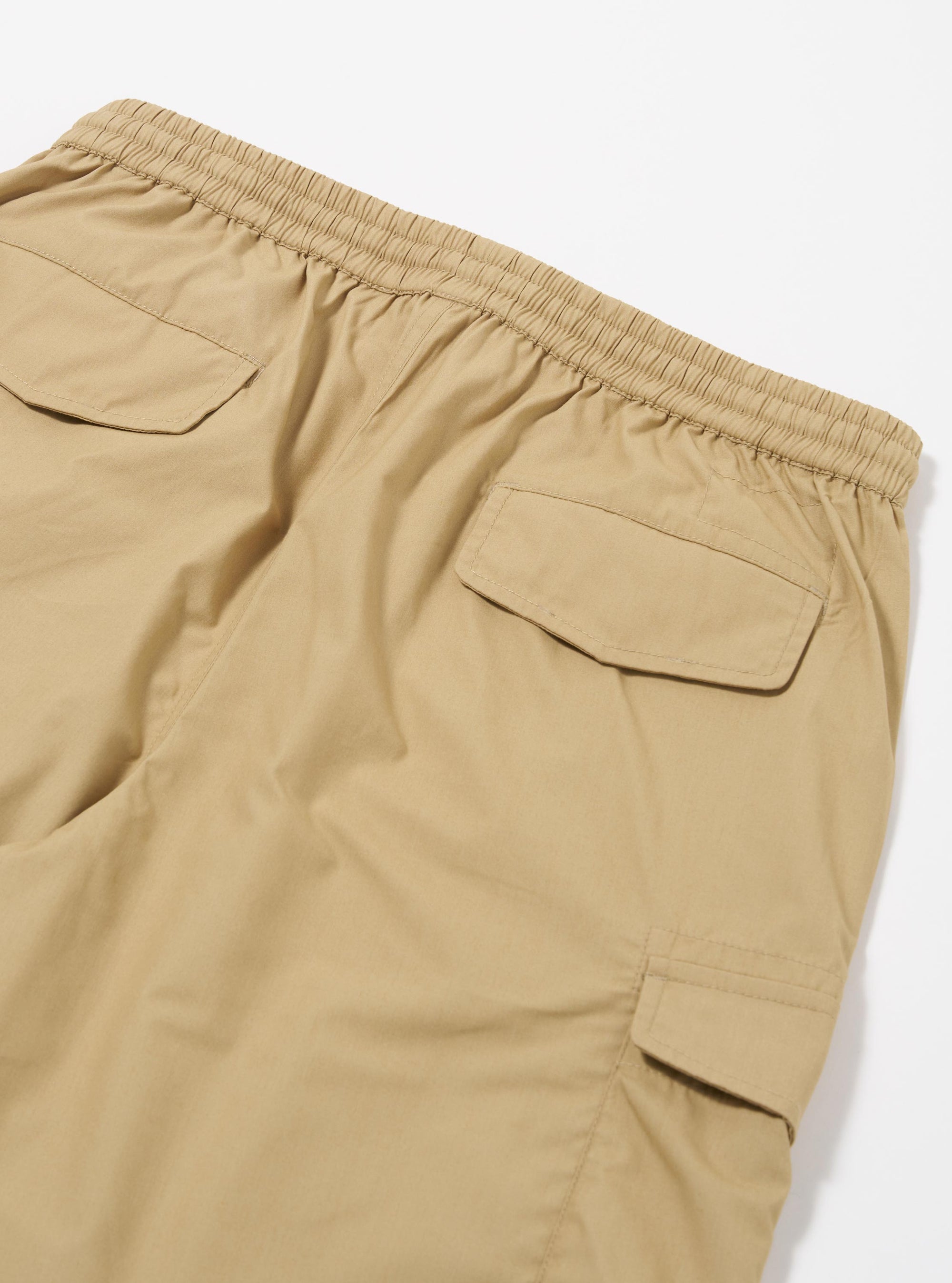 The Sand Recycled Polytech Parachute Short is shown from the back as a flat lay against a plain white background. The image highlights the two rear patch pockets with buttoned flaps, an elasticated waistband, and a drawcord. No model or mannequin is present.