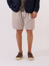 A model wears the Brown Kennedy Stripe Pleated Track Short against a plain white background. The shorts feature a vertical brown and cream striped pattern, a pleated front, and a relaxed fit. The model is shown from the waist down, highlighting the drape of the fabric and the mid-thigh length of the garment.