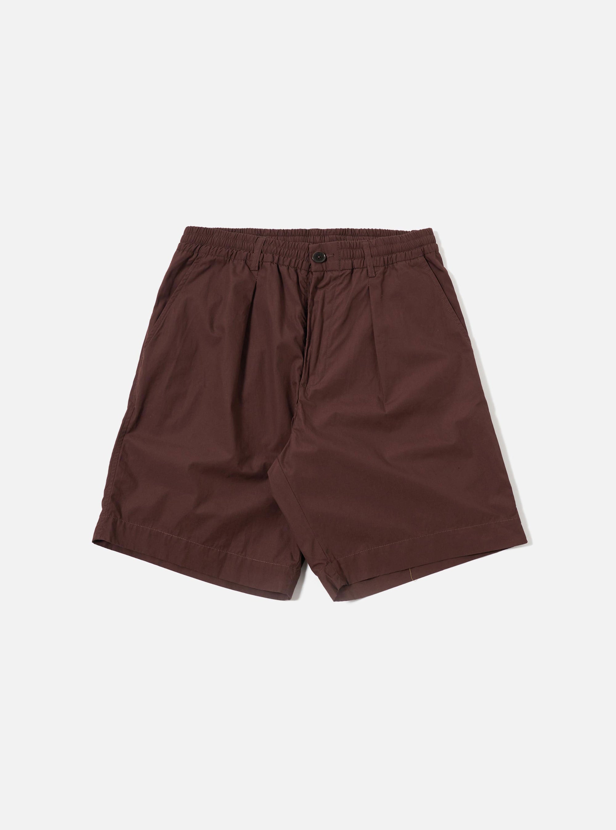 The Brown Peached Poplin Pleated Track Short is shown as a flat lay against a plain white background. The shorts feature an elasticated waistband, a single pleat on each leg, and two large patch pockets on the front. The brown cotton poplin fabric has a smooth, matte finish.