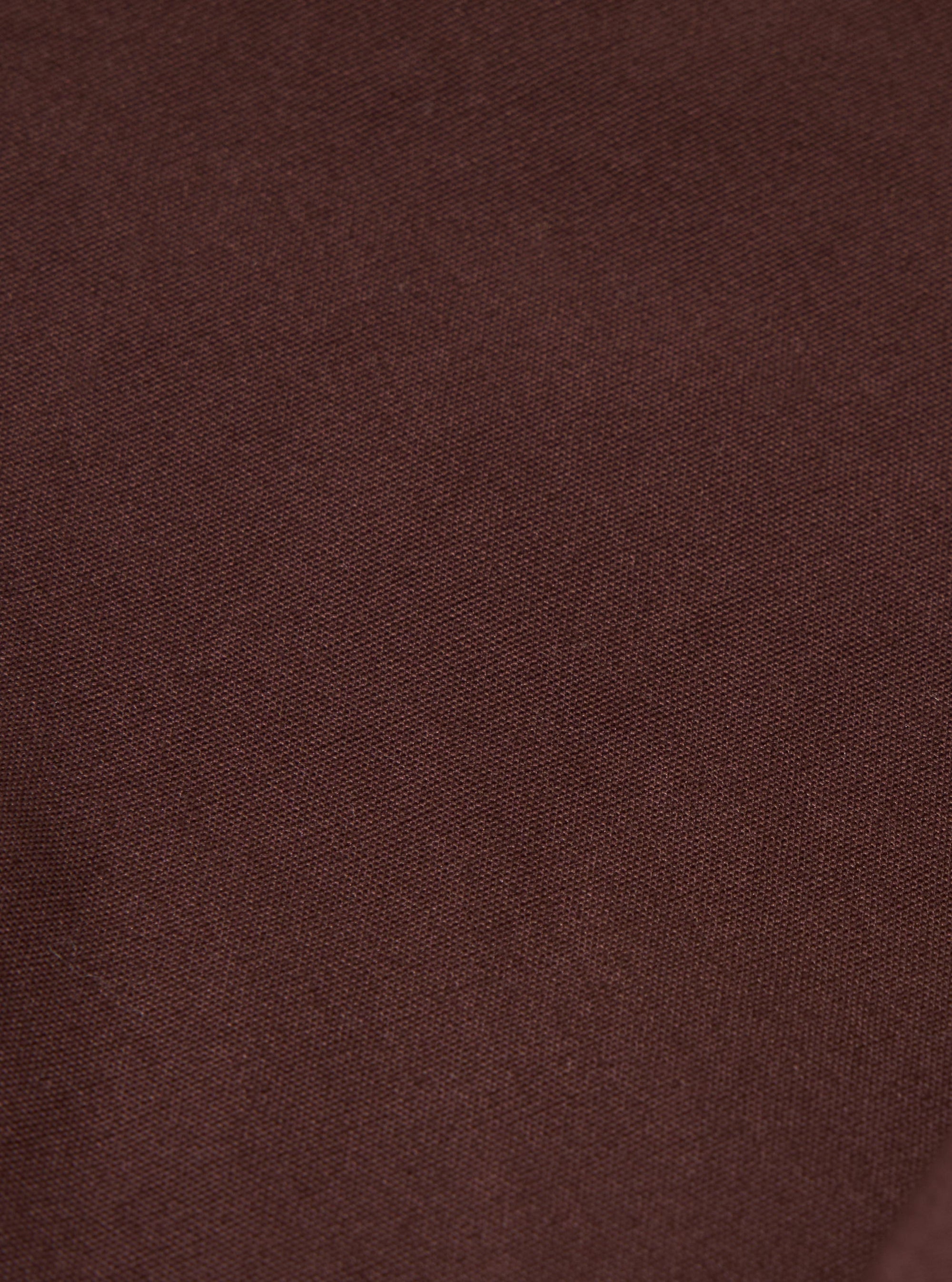 A close-up fabric swatch of the Brown Peached Poplin Pleated Track Short highlights the solid brown color and the soft, slightly brushed texture of the peached poplin material. The fabric fills the frame, providing a detailed view of the weave.