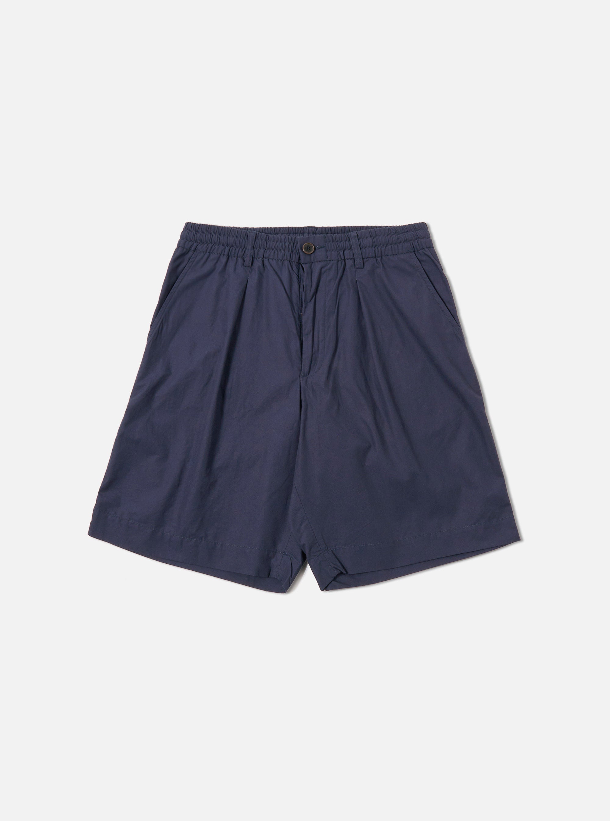 The Navy Peached Poplin Pleated Track Short is shown as a flat lay against a white background. The shorts feature a single pleat on the front, an elasticated waistband with a button closure, and two side hand pockets. The navy cotton fabric has a smooth, peached finish.