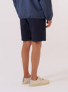 The Navy Dot Waffle Simple Short is worn by a model against a plain white background. The image shows a rear view of the shorts, highlighting the elasticated waistband and the textured dot waffle fabric in navy blue. The model is also wearing a white T-shirt and white socks.