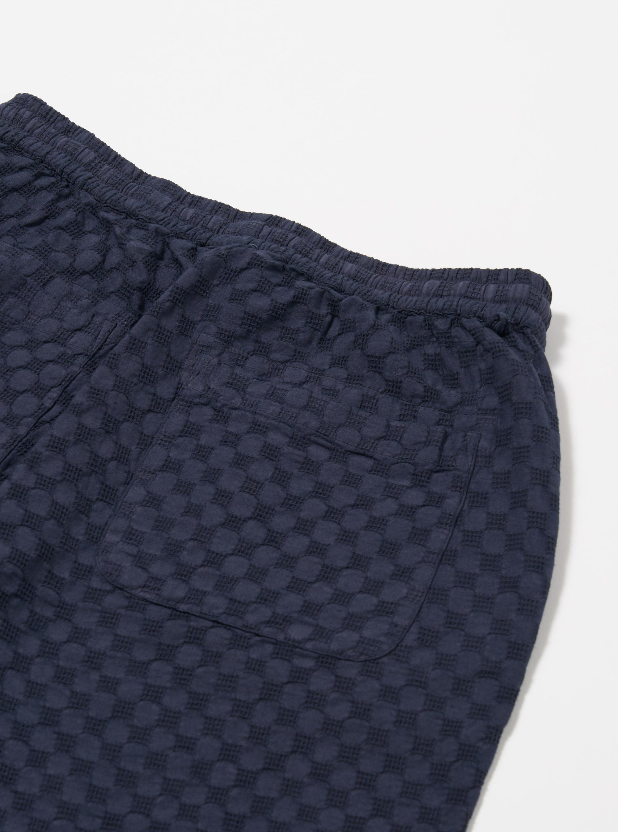 The Navy Dot Waffle Simple Short is shown from the back as a flat lay against a plain white background. The shorts feature a deep navy blue color with a textured dot waffle pattern. The image highlights the elasticated waistband and two reinforced rear patch pockets with visible tonal taping at the openings.