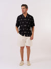 The Black Embroidered Diamond Camp Shirt is shown as a flat lay against a plain white background. The shirt features a camp collar, a button-down front, and a single chest pocket on the left side. The black fabric is decorated with an all-over white embroidered diamond pattern.