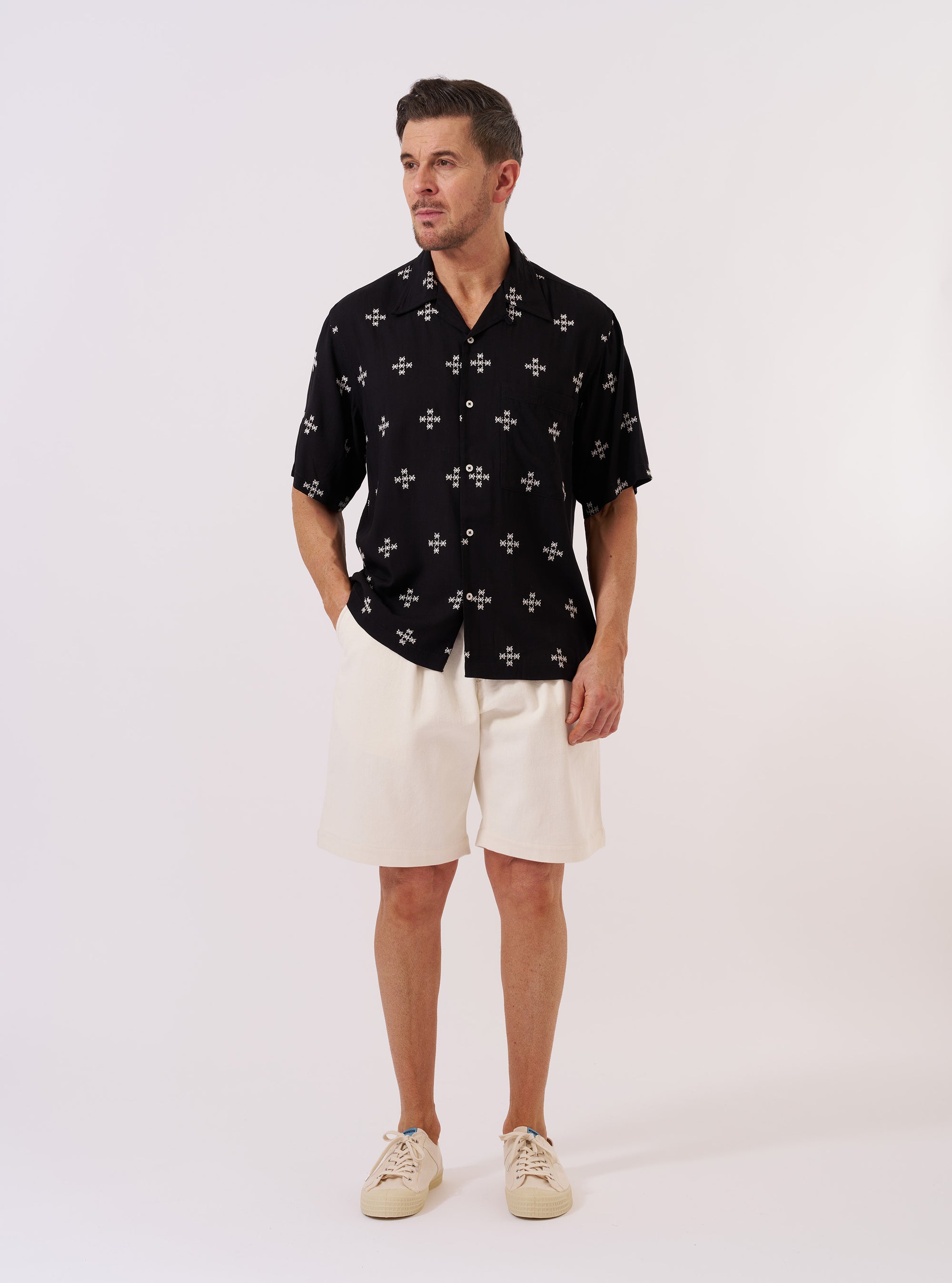 The Black Embroidered Diamond Camp Shirt is shown as a flat lay against a plain white background. The shirt features a camp collar, a button-down front, and a single chest pocket on the left side. The black fabric is decorated with an all-over white embroidered diamond pattern.