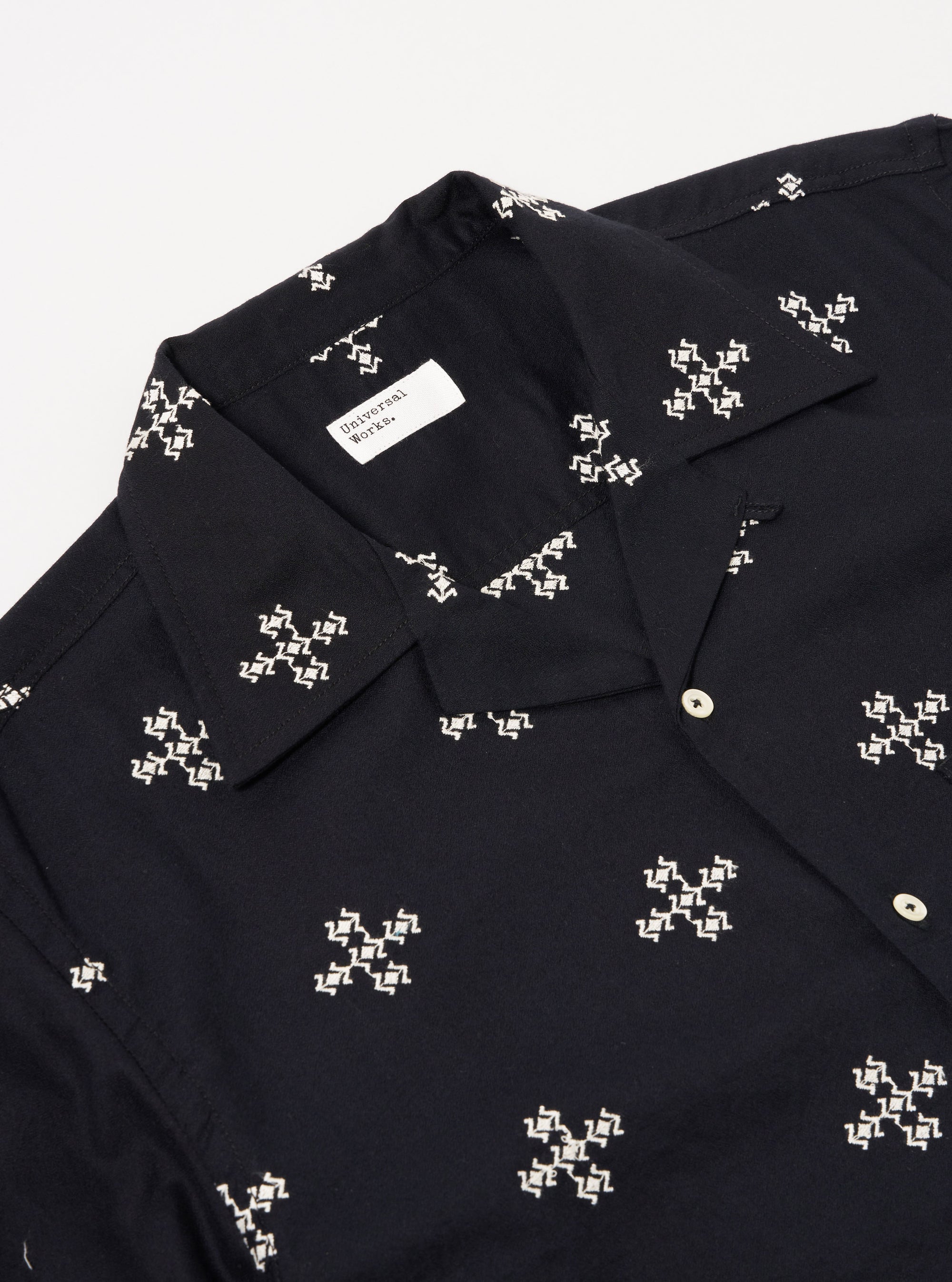 The Black Embroidered Diamond Camp Shirt is shown as a flat lay against a plain white background. The shirt features a camp collar, short sleeves, and two chest patch pockets. A contrasting grey diamond embroidery design is visible across the front panels of the black fabric.