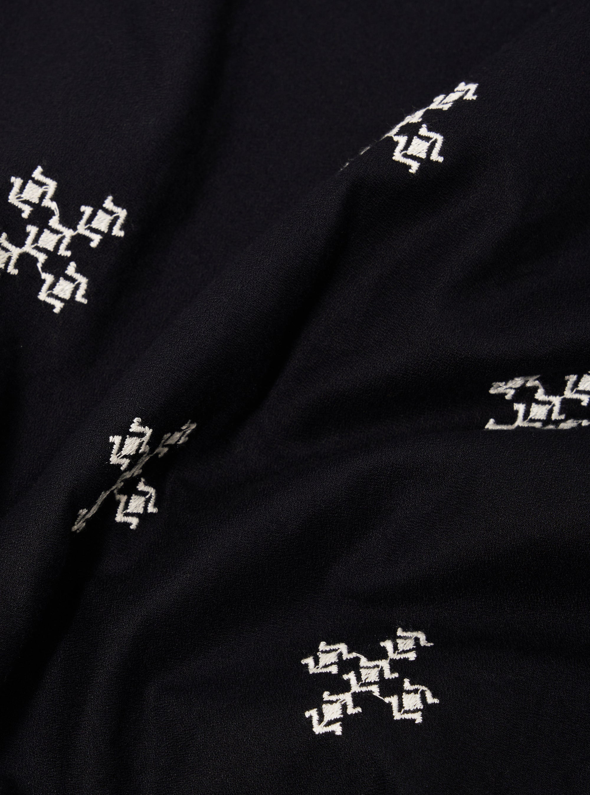 A close-up fabric swatch of the Black Embroidered Diamond Camp Shirt highlights the intricate diamond-patterned embroidery stitched in a slightly lighter thread against the black viscose fabric. The texture of the material and the detailed geometric pattern are the focal points of the image. No model or mannequin is present.