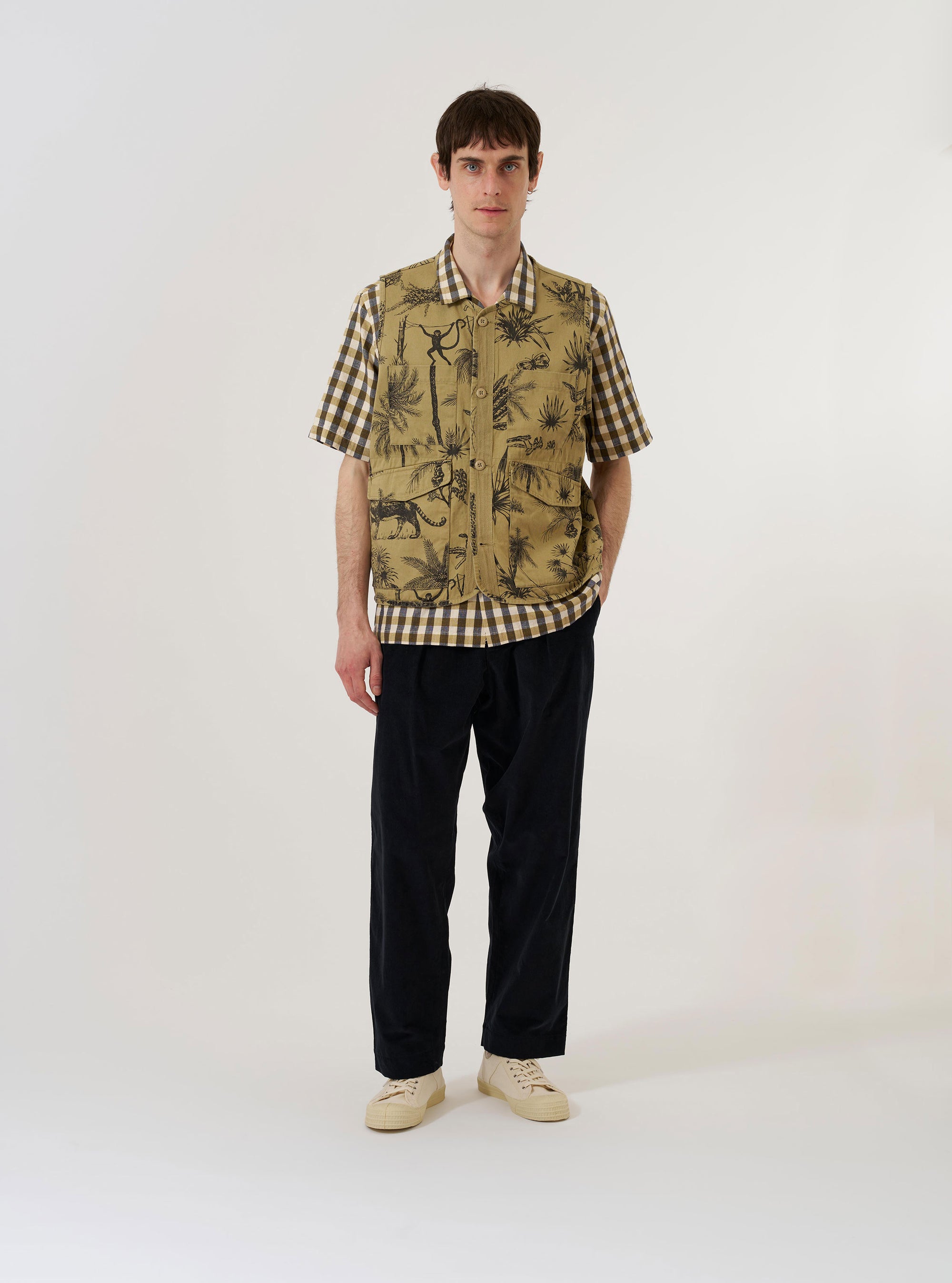 The Sand Jungle Toile Twill 4 Pocket Gilet is shown as a flat lay against a plain white background. The gilet features a detailed jungle-themed toile print in dark ink on a sand-colored base. It has a four-pocket front design, a central button closure, and a structured collar.