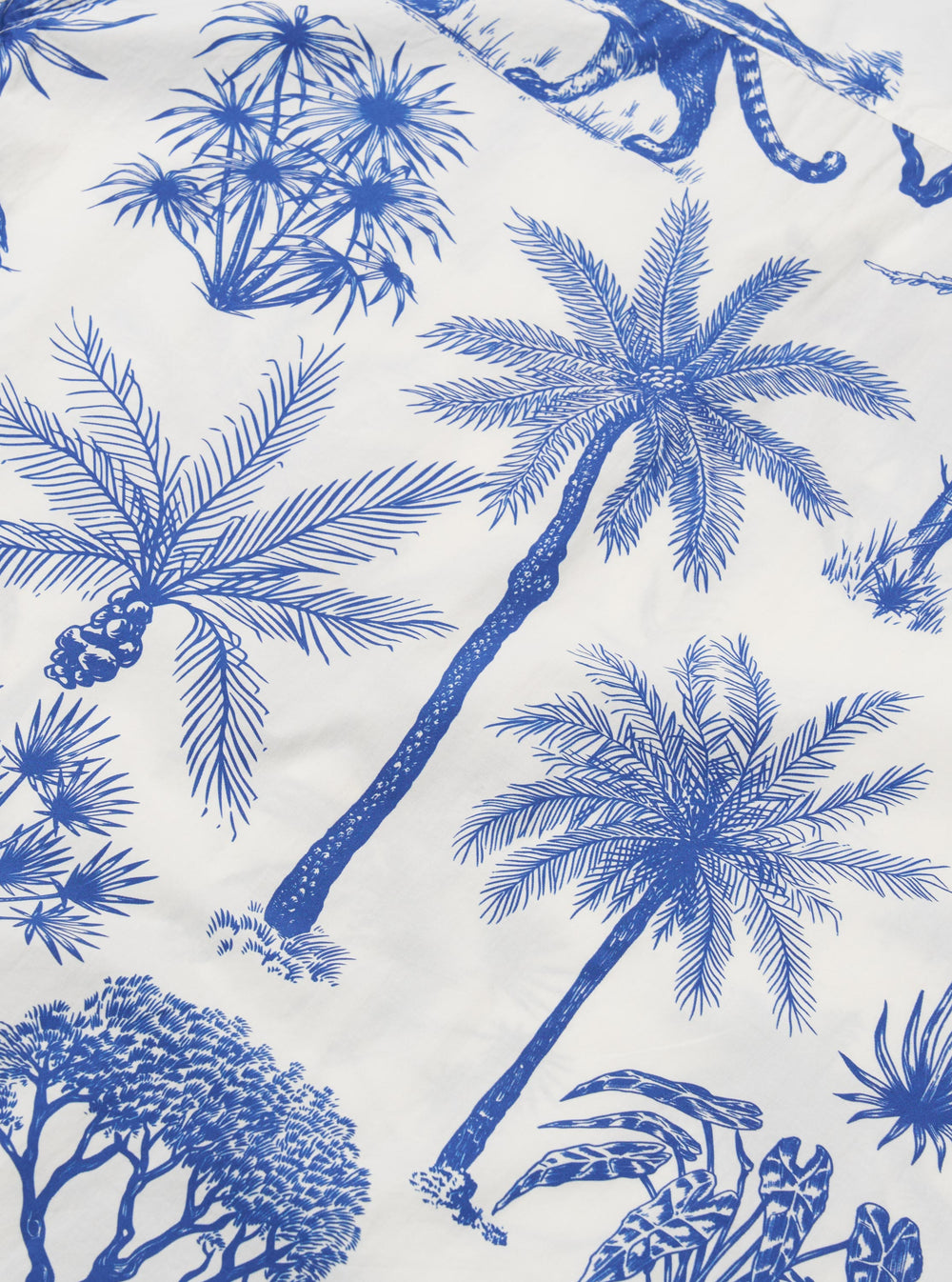 A close-up fabric swatch of the White Jungle Toile Poplin Camp Shirt displays an intricate jungle-themed print featuring animals and tropical foliage in a dark ink against a white cotton poplin background. The image highlights the detailed illustrations and the smooth, lightweight texture of the fabric.
