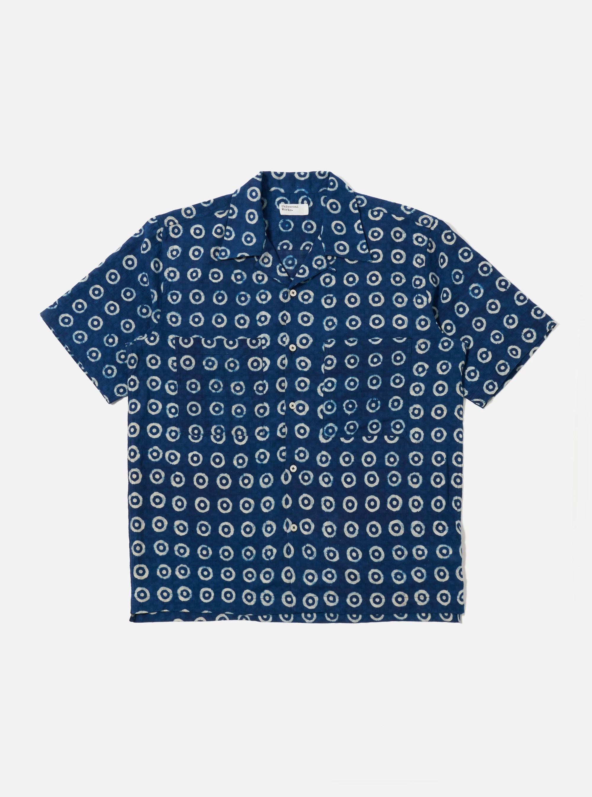 The Indigo Block Print Circles Camper Shirt is shown as a flat lay against a plain white background. The shirt features a relaxed camp collar, a button-down front, and a single chest pocket. The dark indigo cotton fabric is decorated with an all-over white hand-block printed pattern consisting of repetitive concentric circles.