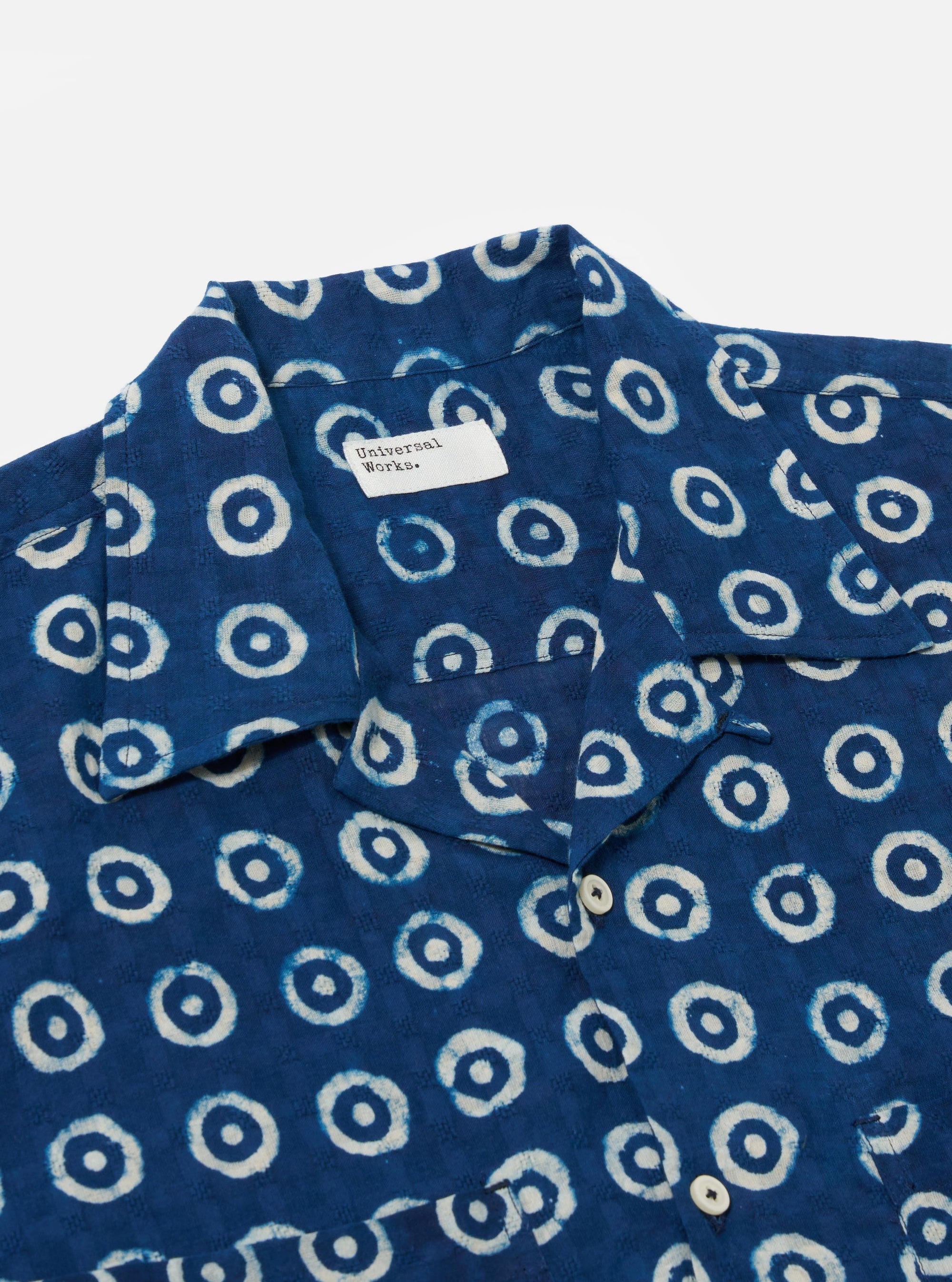 The Indigo Block Print Circles Camper Shirt is shown from the back as a flat lay against a plain white background. The shirt features an all-over white circle pattern on a deep indigo base, a straight hem, and short sleeves. The fabric's block-print texture and the simple construction of the back panel are clearly visible.