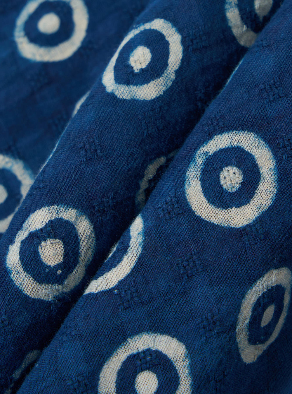 A close-up swatch image of the Indigo Block Print Circles Camper Shirt fabric displays a deep indigo blue color with a repeating pattern of white outlined circles. The texture of the cotton material is clearly visible, highlighting the block print technique.