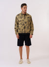 The Sand Jungle Toile Twill Windcheater Jacket is presented as a flat lay against a plain white background. The jacket features an all-over dark jungle toile print on a sand-colored base, a classic collar, and a central zip-front closure. Two large slanted patch pockets are prominent on the front.