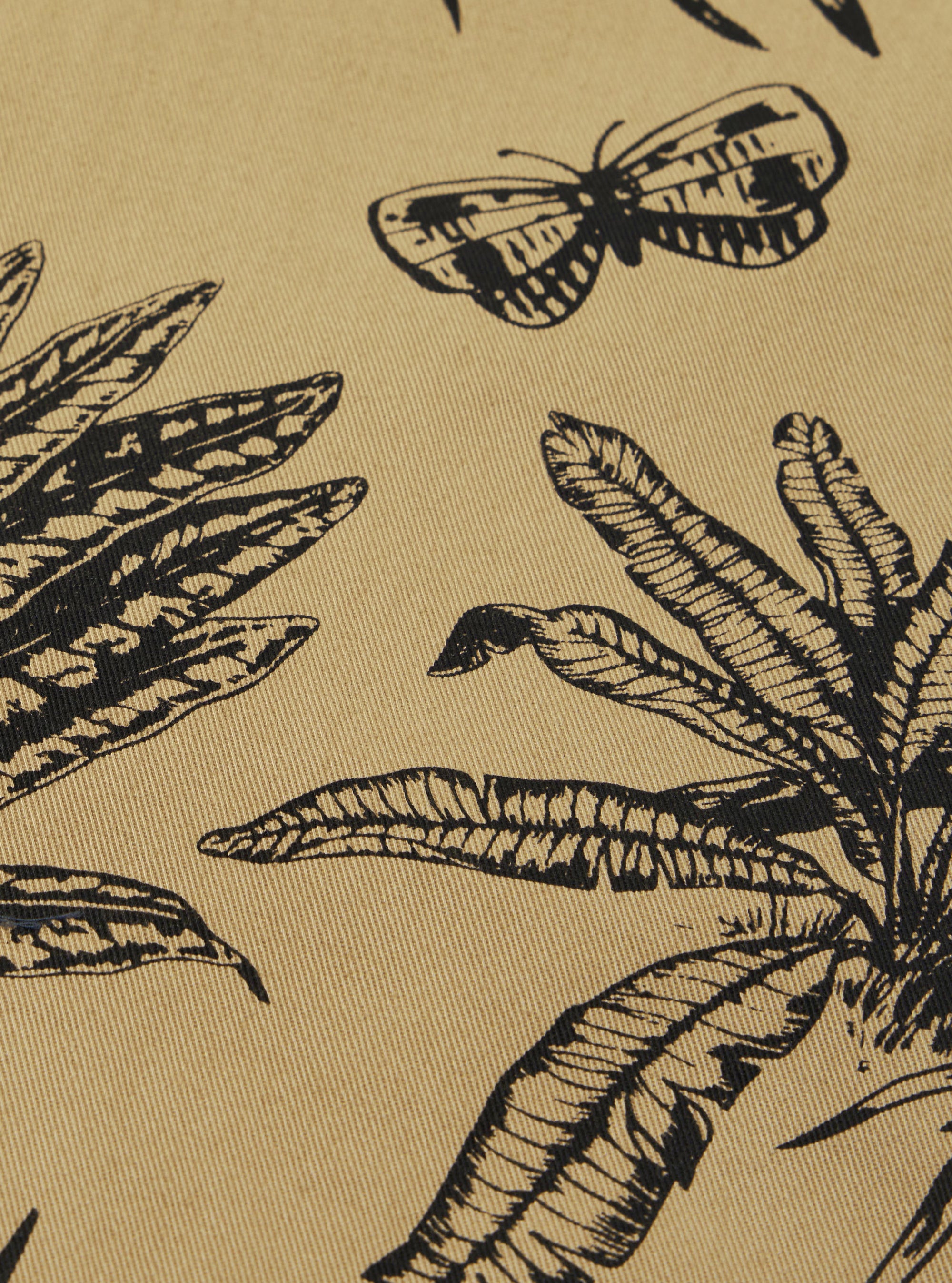 A close-up swatch of the Sand Jungle Toile Twill Windcheater Jacket highlights the detailed jungle toile print featuring animals and tropical foliage in dark ink against a light sand-colored background. The image provides a clear view of the textured diagonal twill weave.