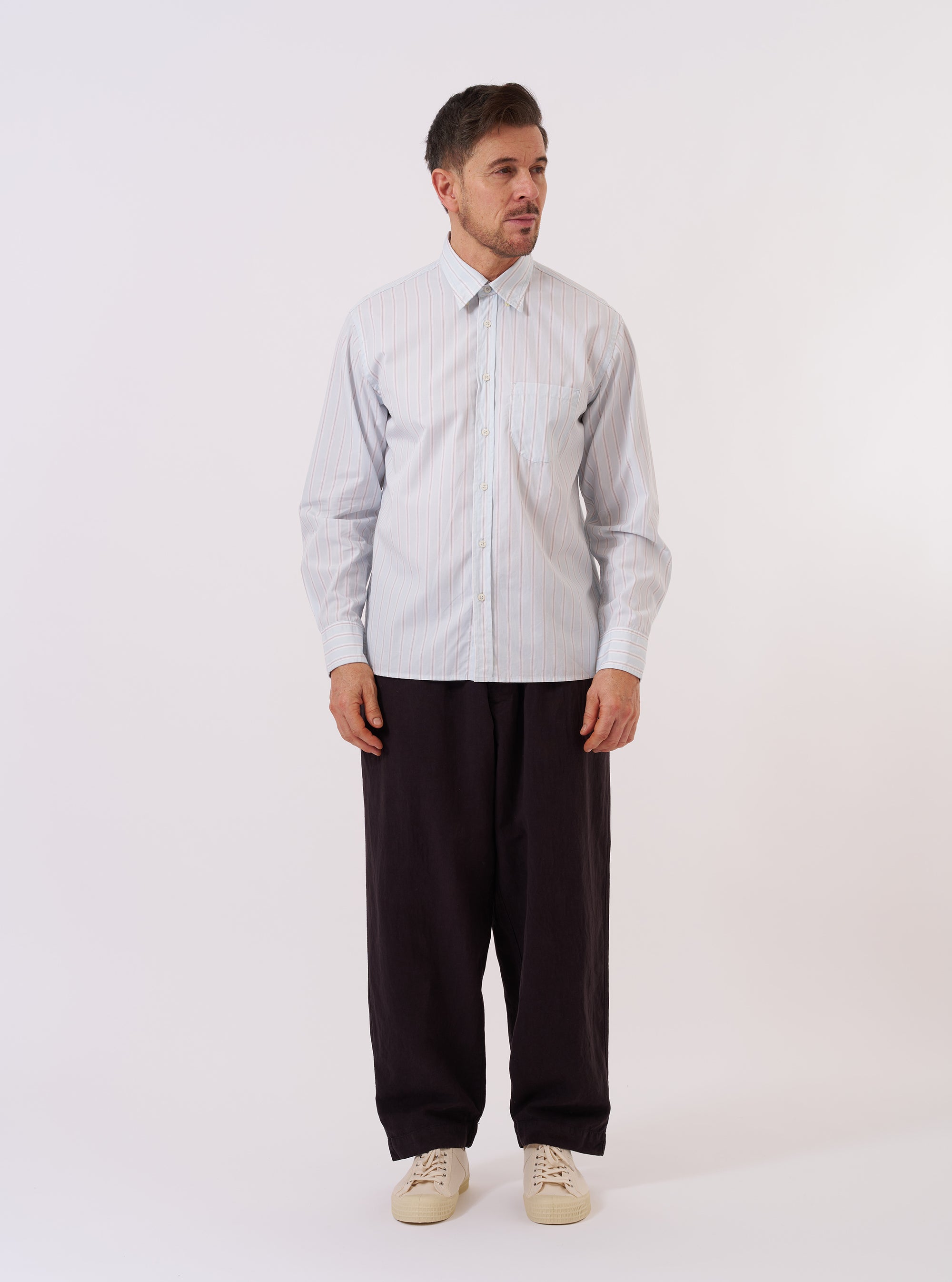 The Sky Urban Stripe Lazy Day Shirt is shown as a flat lay against a white background. The shirt features a light blue and white vertical stripe pattern, a button-down collar, and a single asymmetrical chest pocket on the left side. It has a relaxed fit with a straight hem.