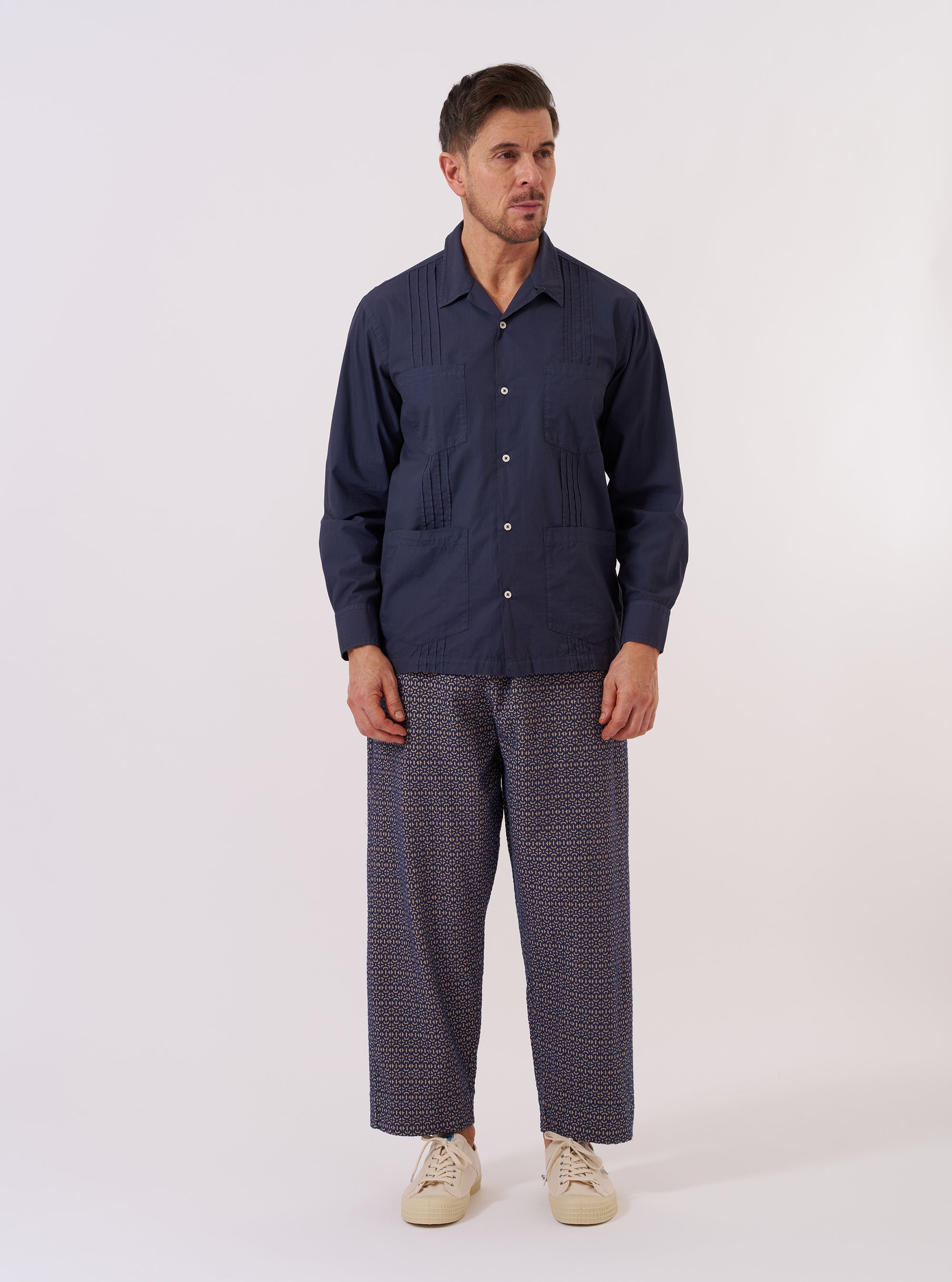 The Navy Poplin Dwight Overshirt is presented as a flat lay against a solid white background. The garment features a camp collar, a full button-down front, and two large utility-style patch pockets on the chest. The navy blue poplin fabric has a smooth, crisp appearance.