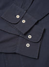 The Navy Poplin Dwight Overshirt is shown in a detail view as a flat lay against a white background. The image focuses on the lower front corner of the garment, highlighting a large patch pocket with a button-down flap and the clean, lightweight texture of the navy blue cotton poplin fabric.